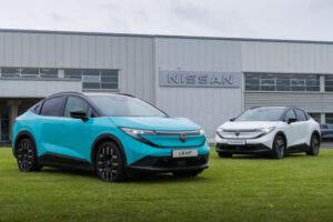 Nissan adds 52kWh battery option to UK-built LEAF Turquoise and white Nissan LEAF electric hatchbacks parked side by side on grass outside a Nissan facility with a large "NISSAN" sign on the building's exterior